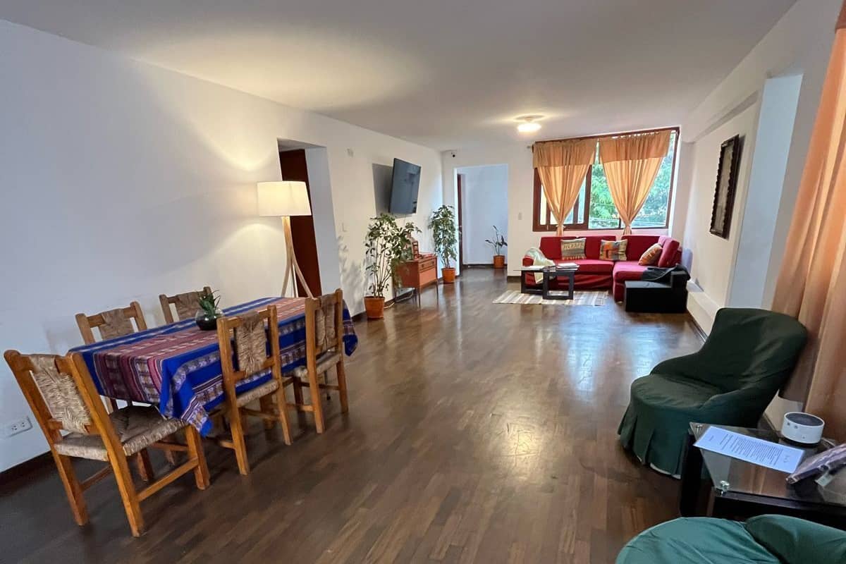 Un salón espacioso con una mesa de comedor de madera y sillas, un sofá rojo y un sillón verde.