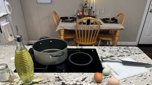 Une cuisine équipée d’une cuisinière, d’une casserole, d’œufs, d’une bouteille et d’une table à manger avec des chaises.