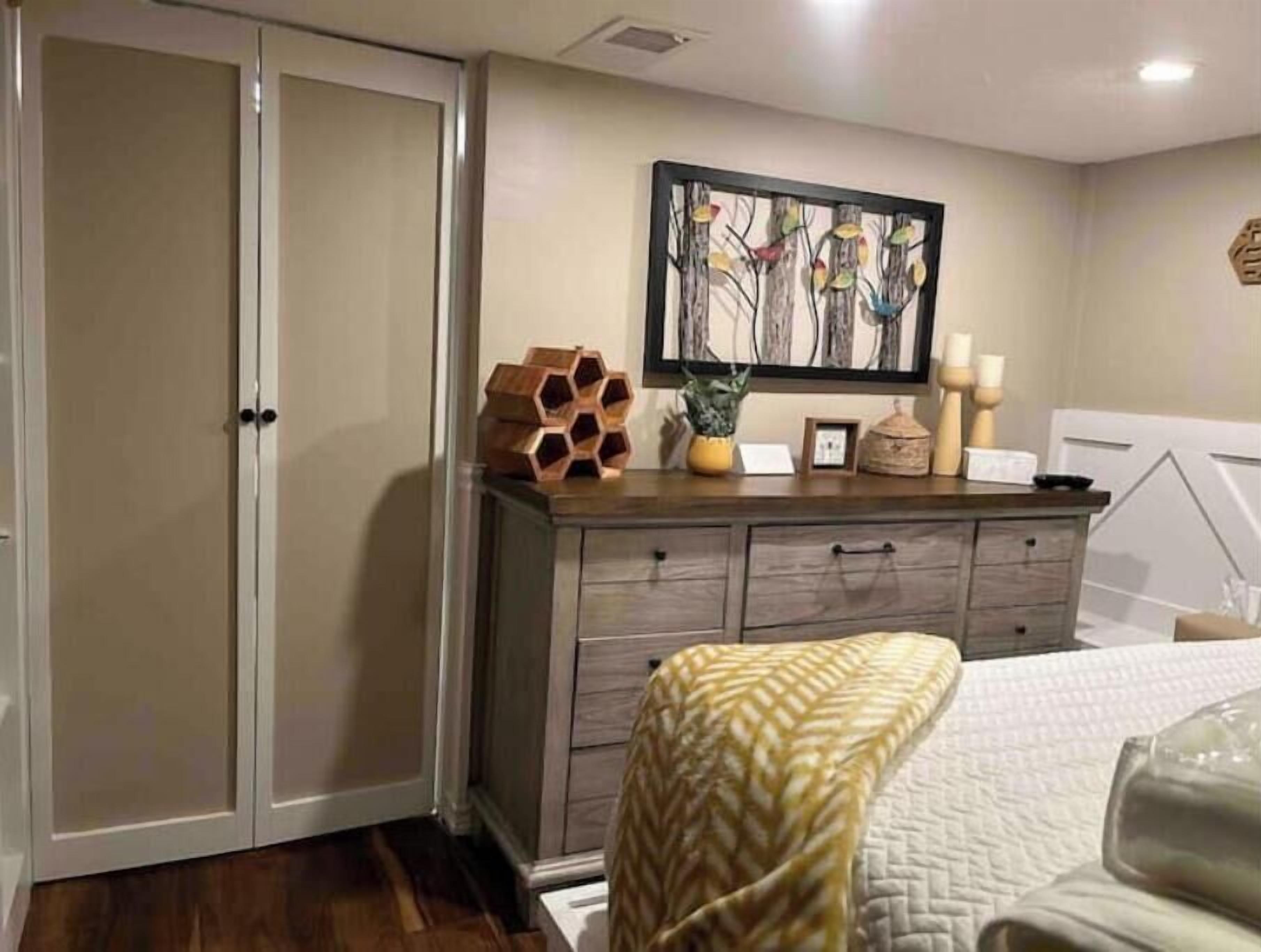 Un dormitorio con cama, cómoda, un cuadro y una escultura de madera sobre la cómoda.