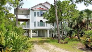A two-story house with a red roof, surrounded by trees and a gravel driveway. - 4C & Sand • Private Pool • Steps to Beach (St. George Island)