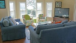 A living room with two sofas, a coffee table, and a television. There are two windows and a door. - 4C & Sand • Private Pool • Steps to Beach (St. George Island)