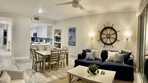 Una sala de estar moderna con un sofá azul oscuro, una mesa de centro de madera y un comedor con una mesa y sillas blancas.