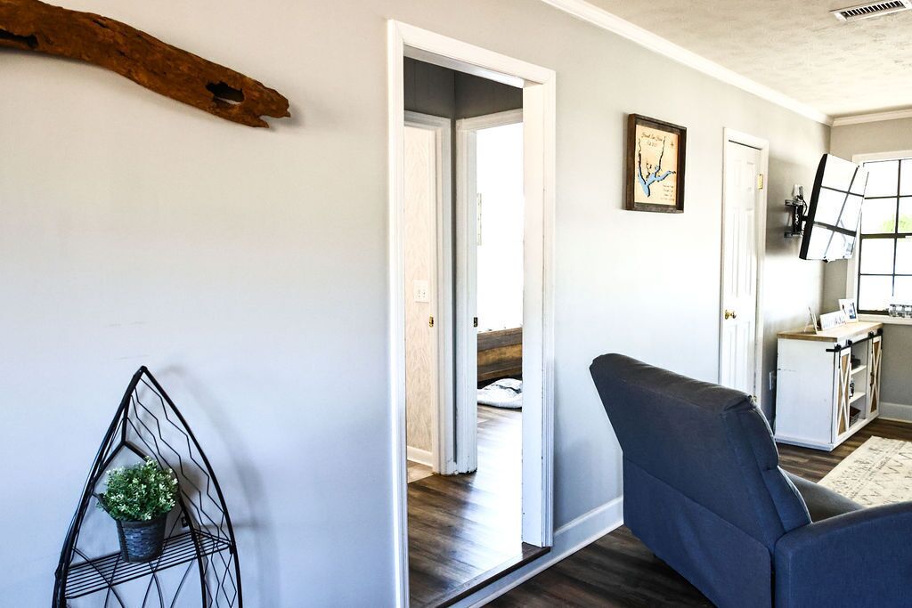 A hallway with a modern chair, a metal plant stand, and a door leading to another room.