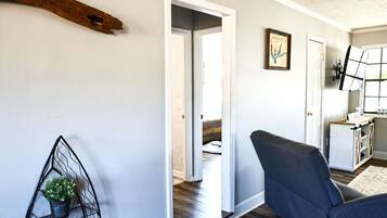 A hallway with a modern chair, a metal plant stand, and a door leading to another room.