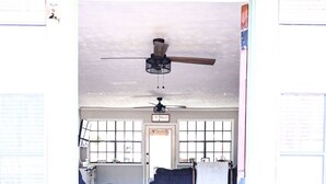 Una habitación con suelo de madera, un ventilador de techo y una puerta que da a otra habitación.