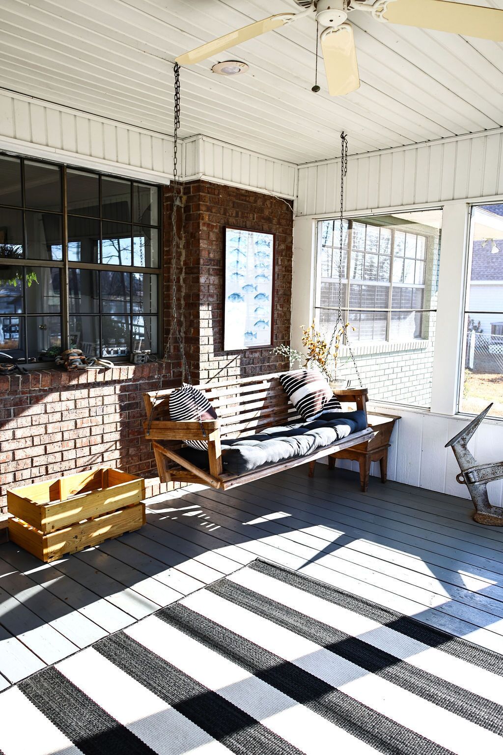 A wooden porch with a hanging swing, a brick wall, and large windows.
