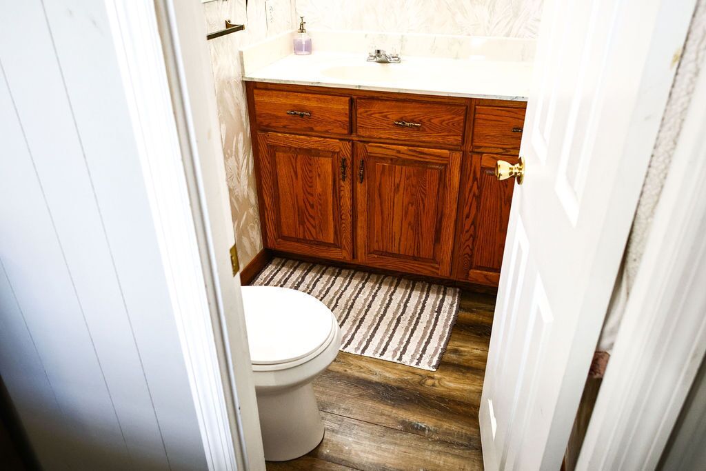 A bathroom with wooden cabinets, a white toilet, and a striped rug.