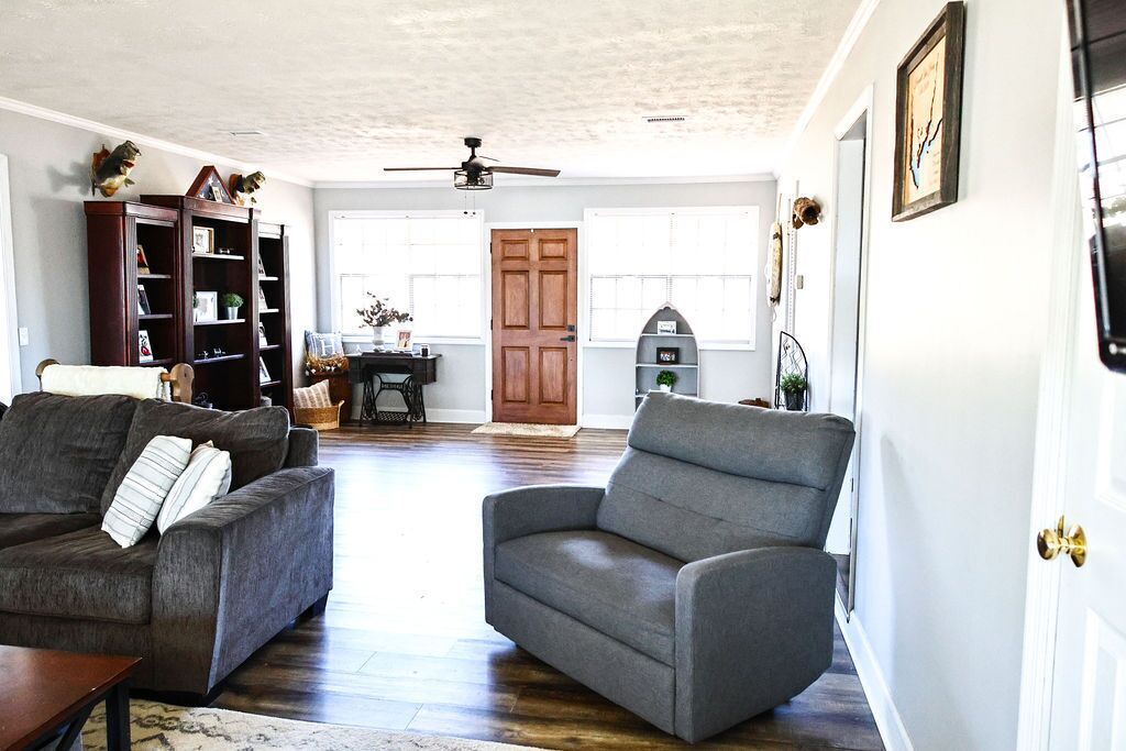 Una sala de estar con un sofá gris, un sillón gris, una estantería de madera y una puerta de madera.