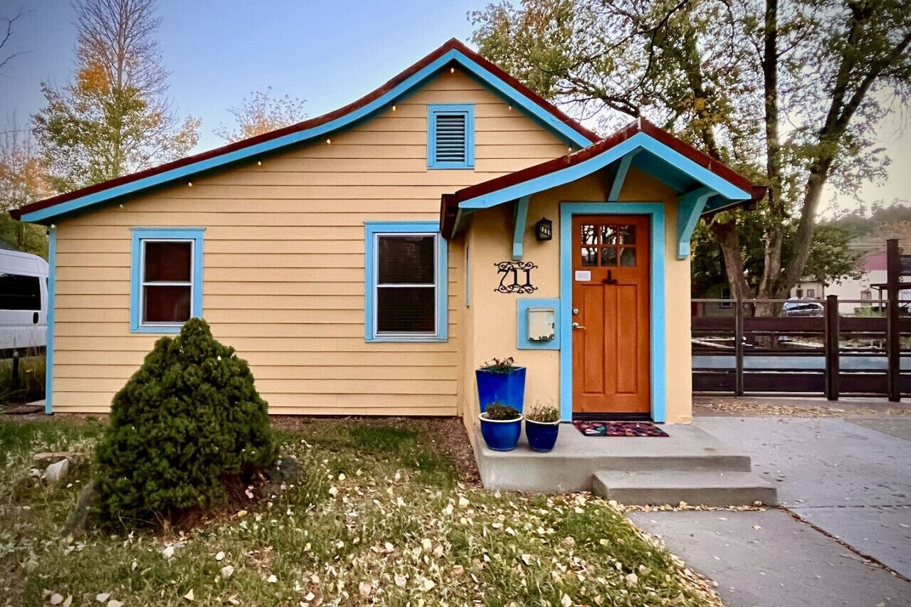 A single-story house with a blue door and windows, a small porch, and a mailbox.