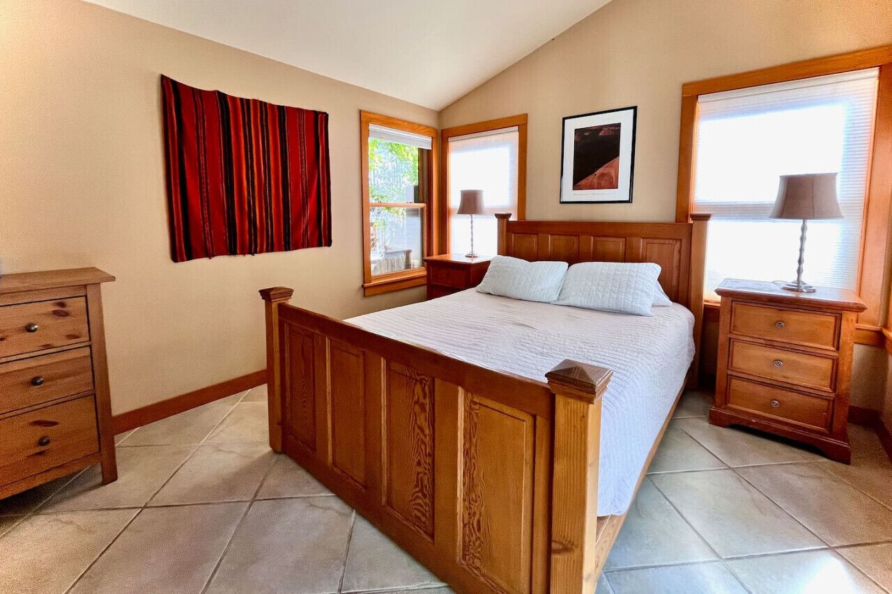 Une chambre à coucher avec un lit en bois, une table de chevet, une commode et une fenêtre avec des rideaux.