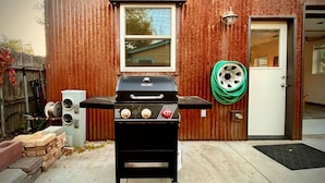 A backyard with a black Weber grill, a wooden fence, a white door, and a hose coiled on the wall. - Joe's Bike Shop w/ Garage and EV Charging (Flagstaff)