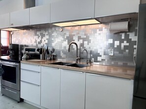 A modern kitchen with a stainless steel range hood, double sink, and white cabinetry.
