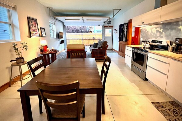 A modern kitchen with white cabinets, a stainless steel oven, and a dining area with a wooden table and chairs.