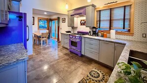 Una cucina con un piano cottura viola, mobili grigi e una finestra con persiane.