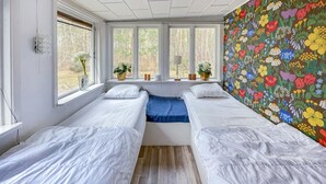 Una habitación con dos camas individuales, una ventana que da a árboles y un papel pintado floral y colorido.