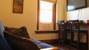 Una sala de estar acogedora con un sofá de madera, un televisor montado en la pared y una zona de comedor con sillas y una mesa.