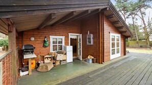 Eine Holzhütte mit überdachter Veranda, Grill und Kühlschrank.