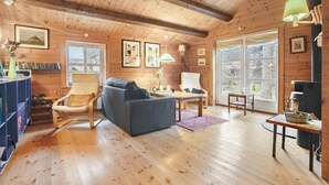 Ein gemütliches Blockhaus mit Holzwänden und Holzböden, einer Couch, Sesseln, einem Tisch und einem Kamin.