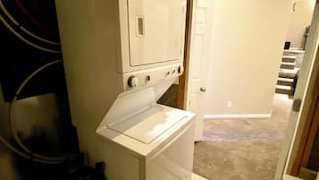 A compact laundry room with a stacked washer and dryer, a green laundry basket on top, and a door leading to a hallway.