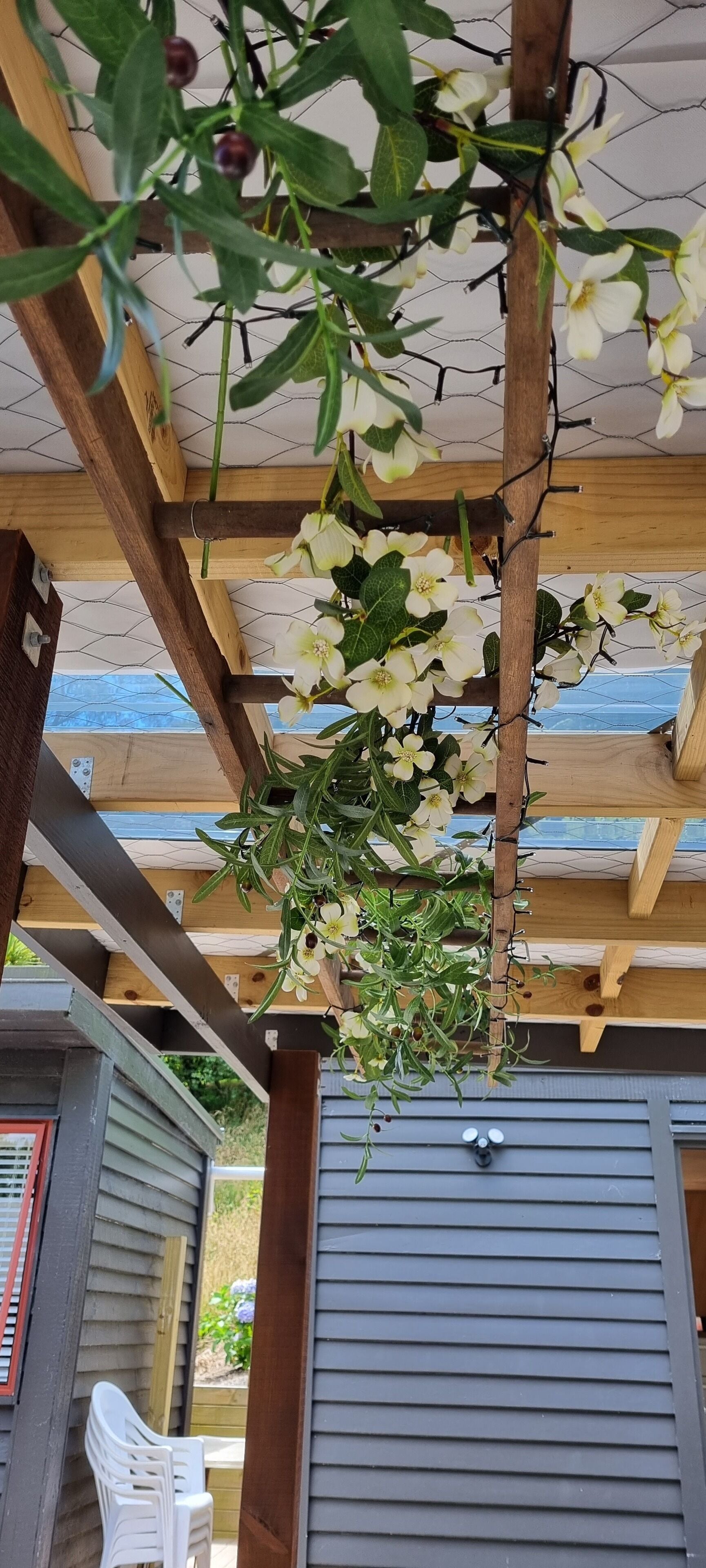 A wooden pergola with white flowers and green leaves.