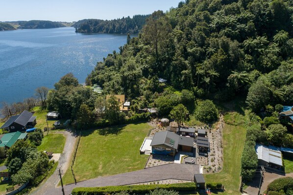 An aerial view of a residential area with a large body of water, dense greenery, and several houses with distinct architectural styles.