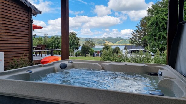Un jacuzzi con vista a una casa, una terraza y montañas al fondo.