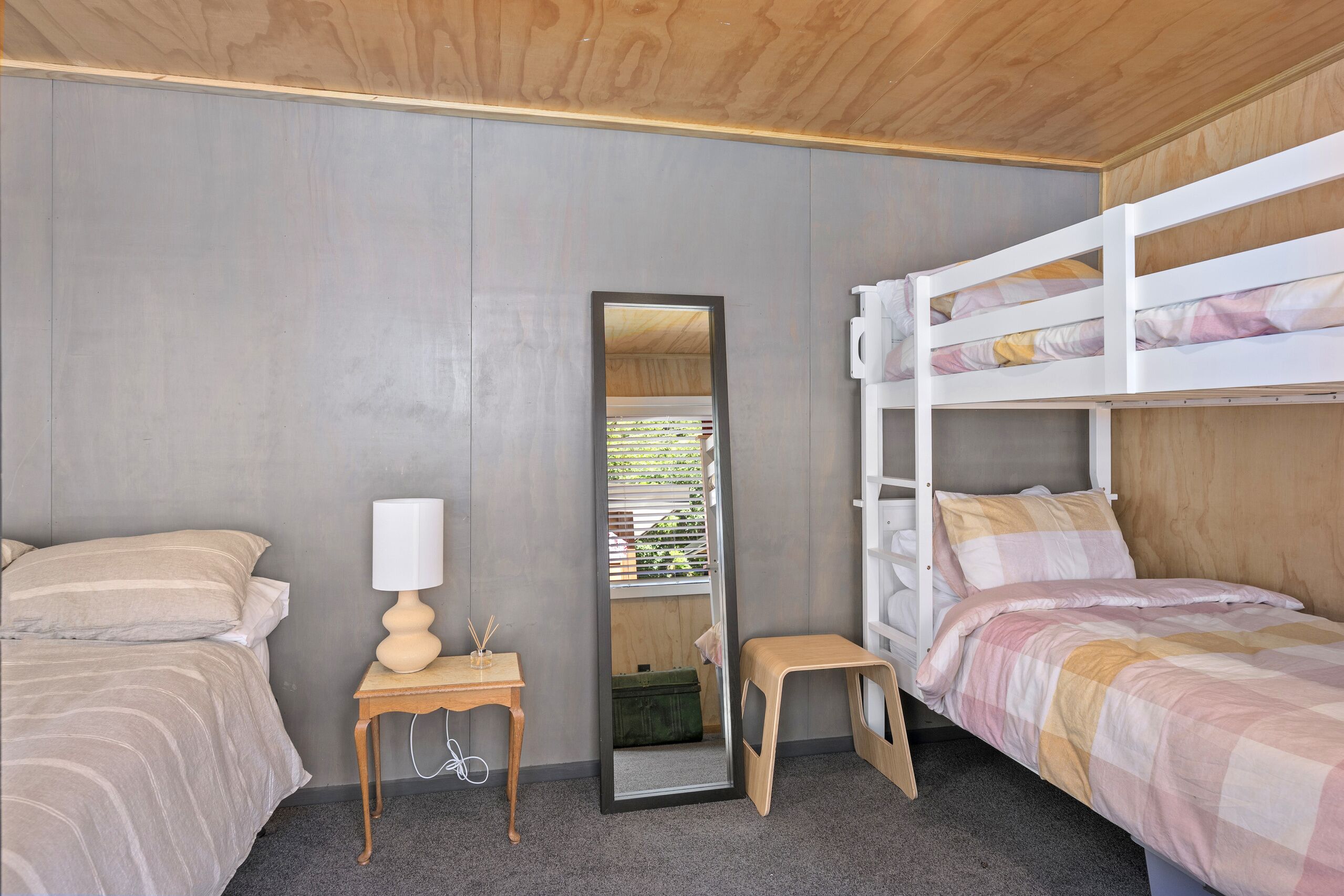 A bedroom with two beds, a mirror, a small table, and a bench.