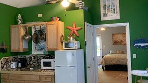 Eine kleine Küche mit Holzausstattung, einem weißen Kühlschrank und einem Deckenventilator. Auf der grünen Wand hängt eine Dekoration mit einem Seestern, und ein Segelboot ist als Gemälde zu sehen.