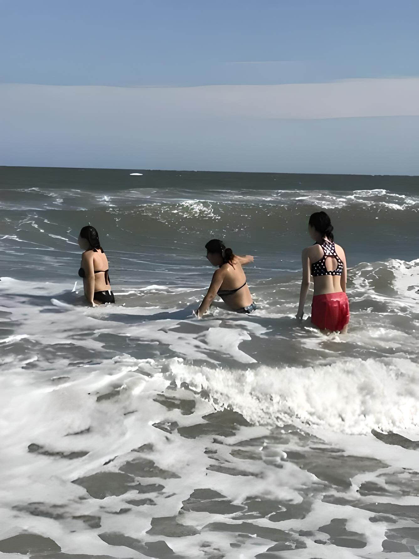 Three individuals in a beach setting with waves and a clear sky.