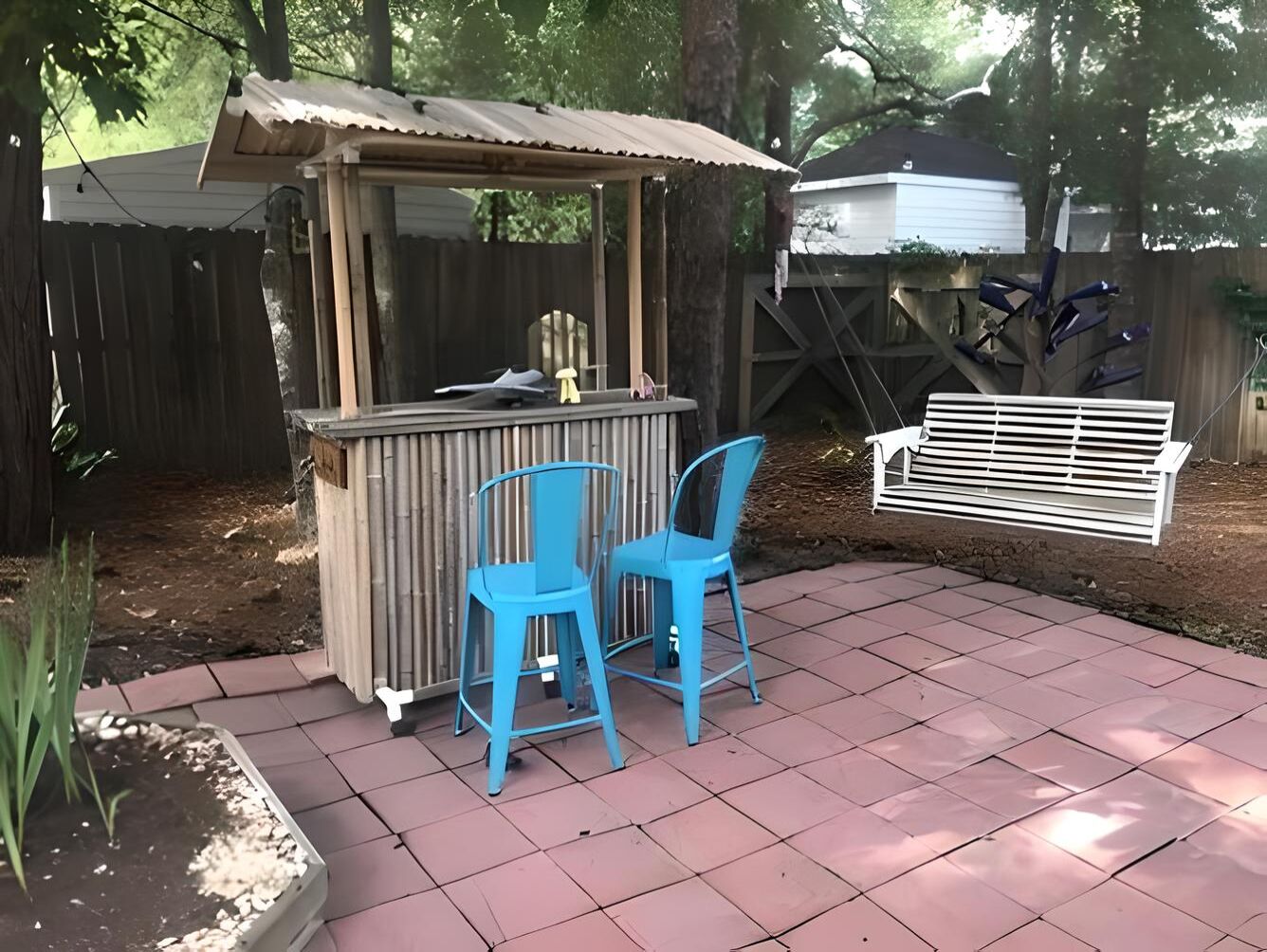 Een terras met een kleine houten constructie, twee blauwe stoelen en een witte bank.