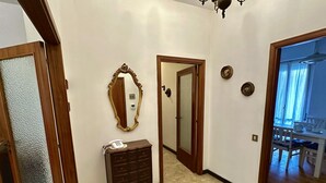 A hallway with a wooden door, a mirror, a telephone on a small wooden cabinet, and a dining area visible through an open door. - S325 - Sirolo, four-room apartment in the center with garden and parking space (SIROLO)
