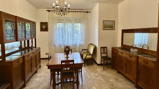 A dining area with a chandelier, wooden cabinets, a table, and chairs. - S325 - Sirolo, four-room apartment in the center with garden and parking space (SIROLO)