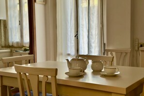 Une table à manger avec des chaises blanches, une théière blanche et deux tasses blanches posées sur la table.