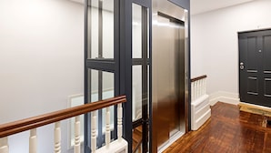 Ein modernes Interieur mit Treppe, Glasaufzug und einer dunklen Tür.