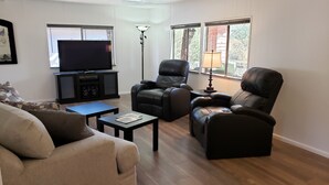 Un salon comprenant un canapé, deux fauteuils inclinables en cuir noir, une table basse, un téléviseur posé sur un meuble et une lampe sur pied.