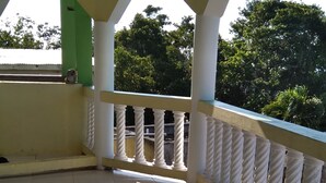 Een balkon met betegelde vloer, witte balustrades en een groene pilaar.