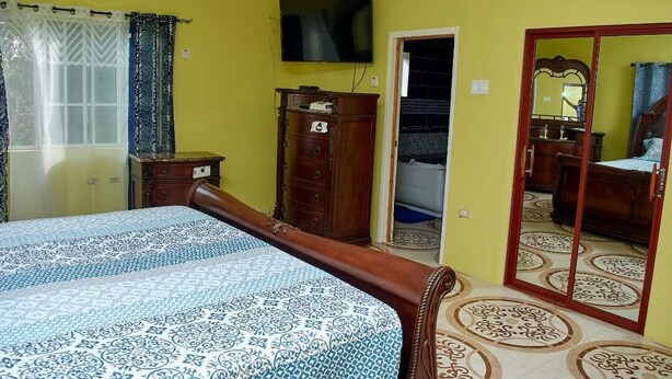 Een slaapkamer met een bed, een dressoir, een televisie en een spiegel.