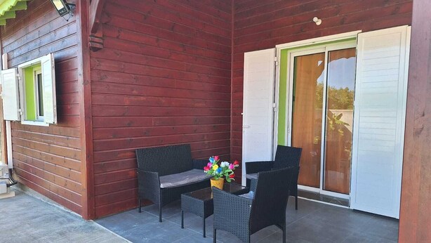 Une terrasse couverte, aménagée avec des meubles en osier et une table décorée de fleurs.