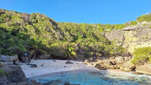 Une plage à l’eau d’un bleu cristallin, bordée d’affleurements rocheux et d’une végétation luxuriante.