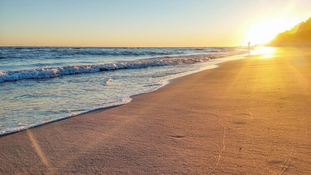Una playa con un atardecer, olas y una estructura distante.