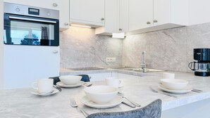 Una cocina moderna con horno empotrado, un lavamanos y una cafetera. Hay cuatro cuencos y tazas blancos en la encimera.