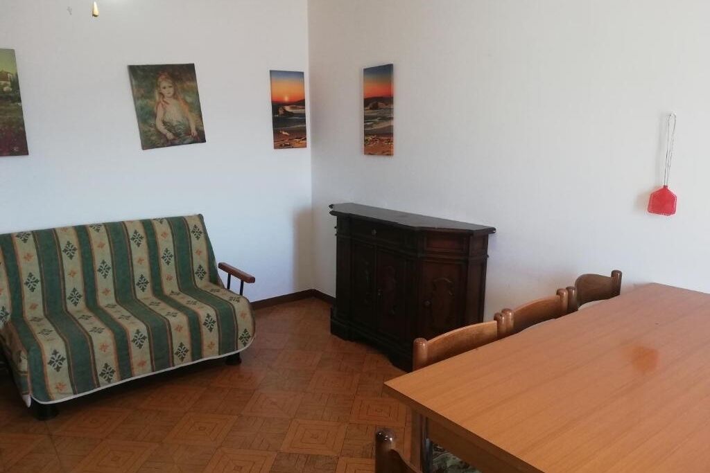 A room with a wooden dining table, a sofa with a patterned cover, a cabinet, and three framed pictures on the wall.