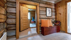 Ein Holzblockhaus-Interieur mit einer Holzbänkl, einem gerahmten Bild an der Wand und einer Tür, die in einen anderen Raum führt.