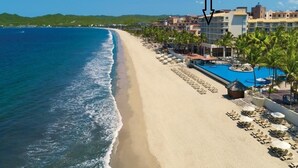 Un resort frente a la playa con piscina, tumbonas y vistas al océano.