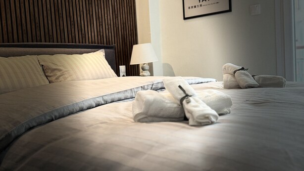 A neatly made bed with towels, a bedside lamp, and a framed artwork on the wall. - KOI Apartment Toumba SKG - Cozy Quality Apartment in Thessaloniki! (Thessaloniki)