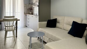 A modern living room with a sofa, a dining table with chairs, a small round table, and a hanging light fixture. - KOI Apartment Toumba SKG - Cozy Quality Apartment in Thessaloniki! (Thessaloniki)