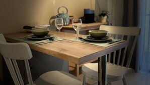 A dining table with a placemat, two bowls, two wine glasses, and a kettle. There are four white chairs around the table. - KOI Apartment Toumba SKG - Cozy Quality Apartment in Thessaloniki! (Thessaloniki)