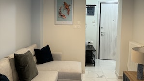 A modern living room with a sofa, a small round table, a hanging light fixture, and a door leading to a bathroom. - KOI Apartment Toumba SKG - Cozy Quality Apartment in Thessaloniki! (Thessaloniki)