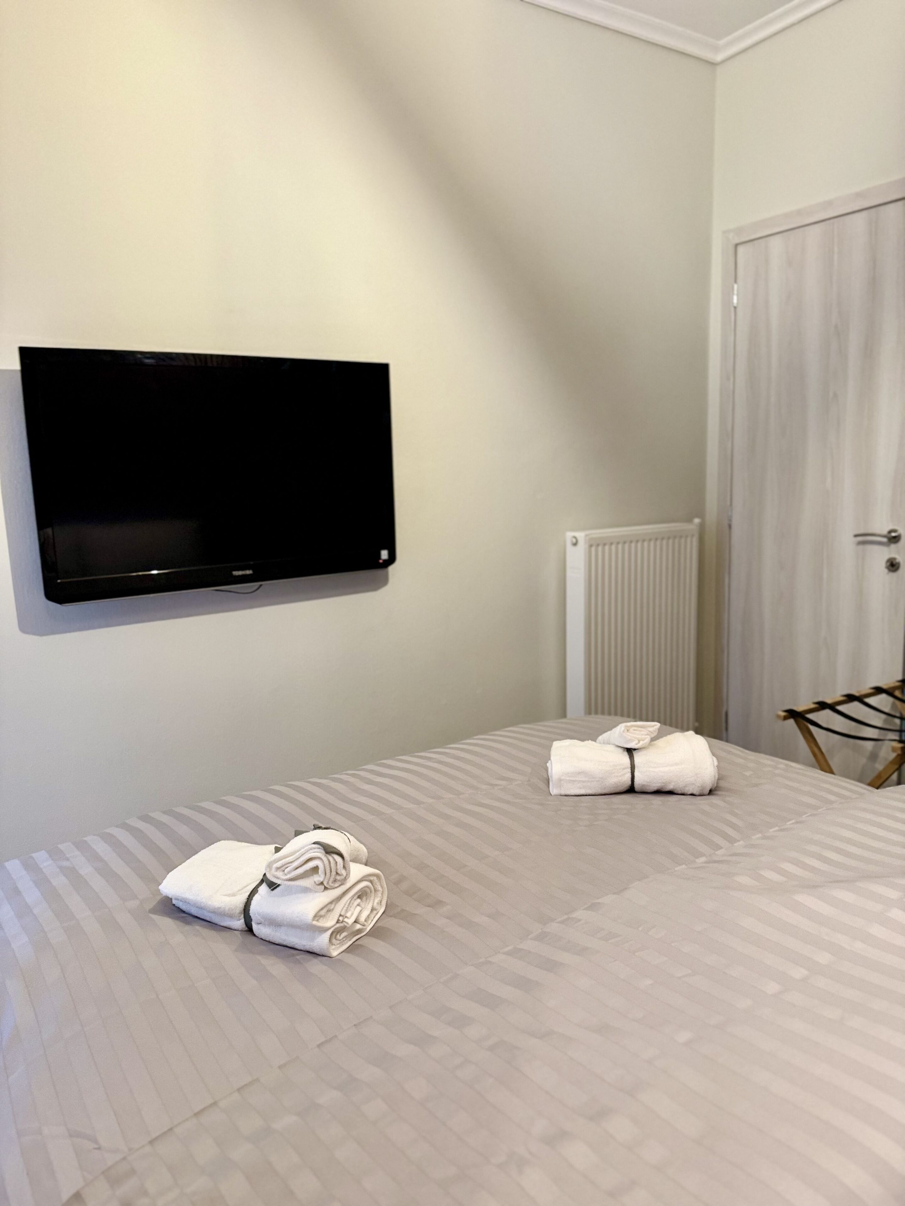 Una habitación de hotel con una cama, un televisor de pantalla plana montado en la pared, un radiador y una puerta.