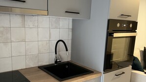 A modern kitchen with a black sink, stainless steel faucet, and a built-in oven. - KOI Apartment Toumba SKG - Cozy Quality Apartment in Thessaloniki! (Thessaloniki)